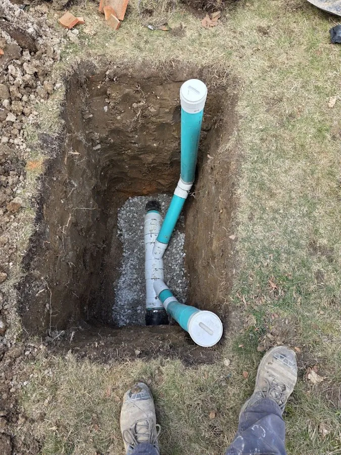Blue drainage pipe installed in yard trench with concrete pads and work site markers visible