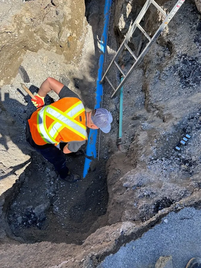 Worker in excavation pit during sewer installation with orange safety warning light