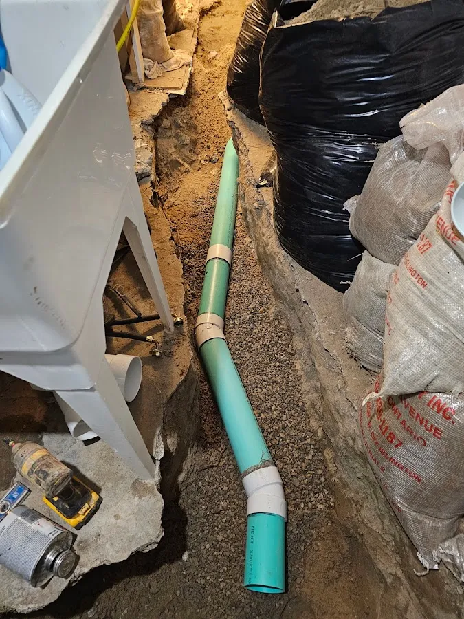 Green sewer pipe installation in foundation trench with protective barriers and gravel base